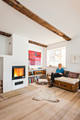 Woman sitting on sofa in bright living room with wooden floor and fireplace