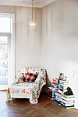 Colourful throw on chaise chair and stacks of books in corner