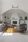 Armchair with grey cushions, matching sofa and coffee table in front of fireplace in white-painted log cabin