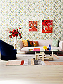 Upholstered sofa, side table with bouquet of roses, armchair and coffee table in the living room with floral wallpaper, pictures on the wall