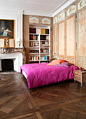 Old parquet floor and fitted wardrobes in bedroom with hot-pink bed linen on double bed