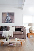 Helles Polstersofa mit Kissen, darüber Bild mit Buddha-Motiv im Wohnzimmer