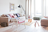 Sofa mit Kissensammlung und Rattanstuhl im Wohnzimmer in Pastelltönen