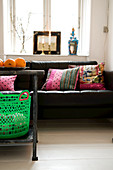 A plastic basket on a metal table in front of a leather sofa with patchwork cushions