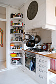 Kitchen utensils on corner shelves next to the cooker with masonry mantel hood