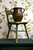 ceramic vase on a green old children's chair in front of wallpaper with a floral motif