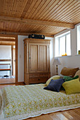 Bett mit Samtkissen in Naturtönen im ländlichen Schlafzimmer mit Holzdecke