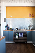 Blue-grey base units and yellow wall in kitchen-dining room