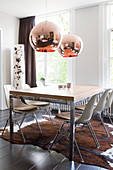Dining table with classic chairs on a fur rug, with copper pendant lights hanging from the ceiling