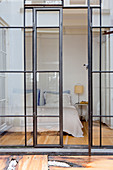 Double bed in bedroom seen through industrial-style glass wall and doors