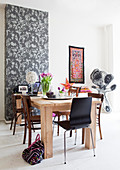 Solid wood table with various chairs in front of wallpaper with a floral pattern