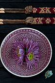 Purple chrysanthemums (Chrysanthemum) on an ornately patterned plate