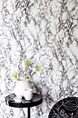 Black side table with a vase in front of marble print wallpaper