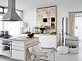 Kochinsel, weißer Designerstuhl, Lederpoufs und Sideboard in offener Küche