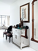 Mirrored dresser with African sculptures and dark rococo chairs in the entryway
