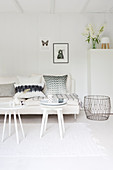 White couch with pillows, side tables, and metal basket in a white living room