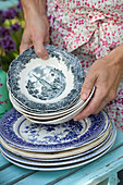 Hands holding stack of old plates and bowls with classic pattern
