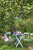 Flowers on set table below tree in summery garden