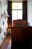 Decorative writing on an old wooden bed in a narrow room with a dotted wall paper