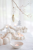 Weiße Holzperlenkette und Teelichter auf Weihnachtstisch, darüber Zweig mit Baumschmuck