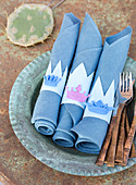 Homemade napkin rings with small crowns on blue napkins