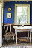 Alter Stuhl und Tisch vorm Fenster und zweifarbiger Bretterwand