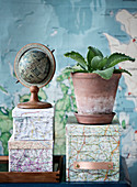 Globus und Brutblatt auf mit Landkarten beklebten Schachteln