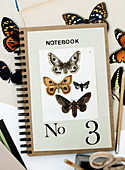 Postkarte mit Schmetterling-Motiven und Zahl 3 auf einem Notizbuch