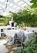 Esstisch mit Stühlen und Bank und Grünpflanzen auf überdachter Terrasse