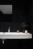 A white washbasin against a black wall in a bathroom