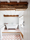 Weißes Badezimmer mit Holzbalken, frei stehender Badewanne und Fliesenboden in renoviertem Bauernhaus