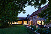 Altes Bauernhaus mit Terrasse und moderner, beleuchteter Anbau mit Glasfront