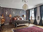 Double bed with antique bed head flanked by floor lamps and gold coloured statue in bedroom