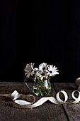 Coiling ribbon placed on timber tabletop near glass vase with white flowers on black background