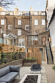 Grey seating on terrace in courtyard surrounded by urban brick houses