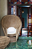 Cane peacock chair on terrace outside open stained-glass doors