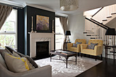 Pastel armchairs and coffee table in living room with black-painted chimney breast and staircase in background