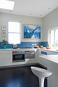 White fitted kitchen with blue splashback and barstool at counter