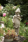 Flower fairy statue next to roses and Jenny's stonecrop planted in bowl