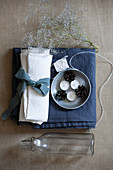 White linen napkin with blue ribbon, tealights, pine cones, yarn, flowering twigs and swing-top bottle