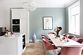 Dining table and chairs in open-plan kitchen with white cupboards and pale grey wall