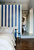 Bed room with doorway leading into raised bathroom behind blue-and-white striped partition wall in small apartment