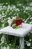 Small bouquet with apple blossoms, parrot tulips and red daisies on a side table in the meadow