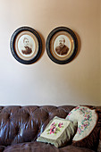 Scatter cushions on vintage leather couch below old photos on wall