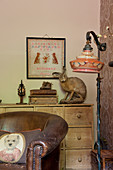Scatter cushion on vintage leather armchair and standard lamp in front of stuffed hare on top of chest of drawers