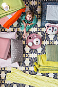 Child sitting on patterned rug surrounded by blankets