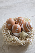 Brown hens' eggs painted with white patterns in Easter nest made from raffia and Iceland moss
