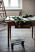 Efeuranken, Stoffblumen und Bastelmaterialien auf altem Tisch