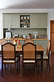 Grey-green dresser and cane-backed chairs around dining table in kitchen-dining room