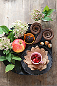 Herbstliche Tischdekoration mit Apfel, Hagebutten, Hortensienblüten und Widderzapfen